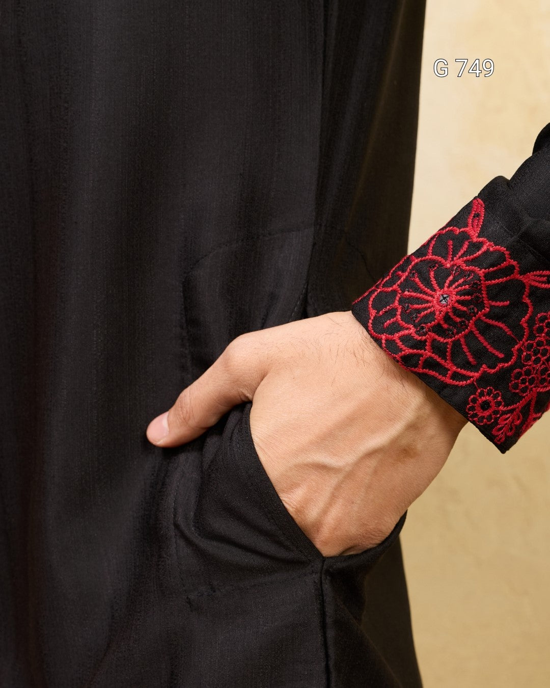 Close-up of a person wearing a black garment with red floral embroidery on a beige background