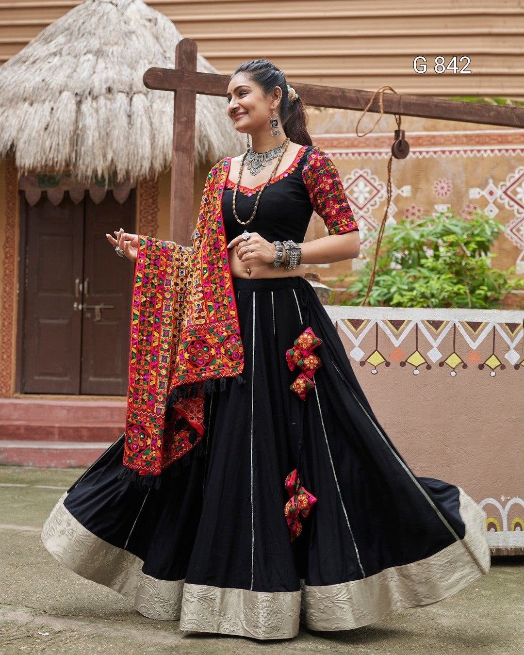 Woman in a traditional black and red outfit with a colorful shawl outdoors.