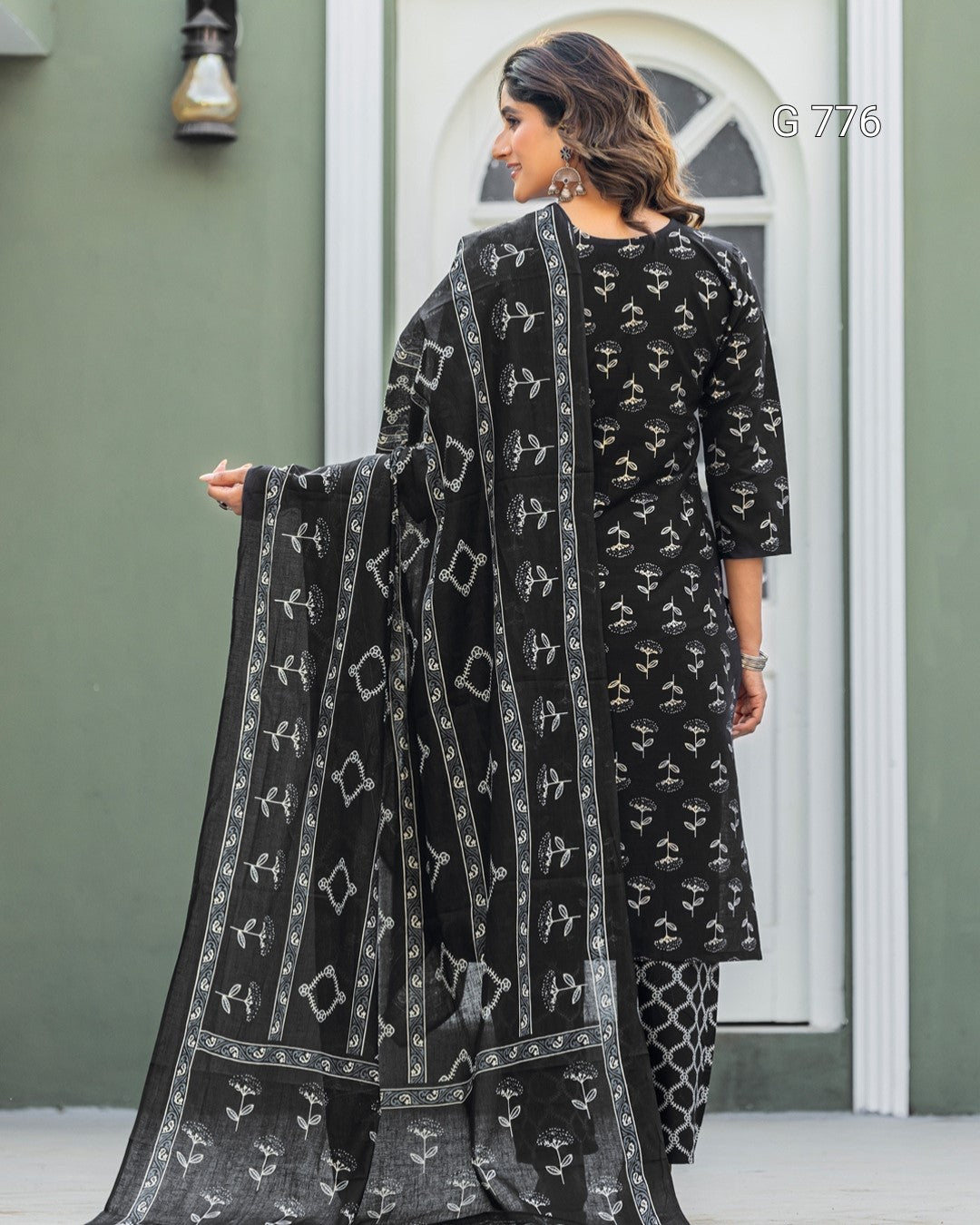 Woman wearing a black and white patterned outfit with a matching dupatta, standing against a green wall.
