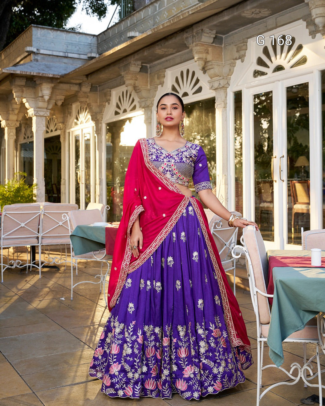 Woman in a traditional purple and pink outfit standing outdoors near a building.