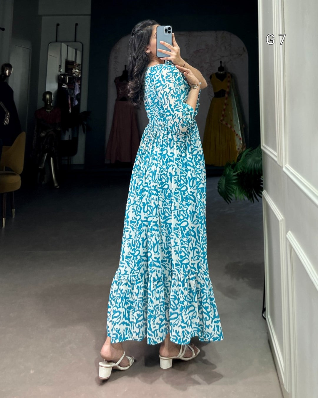 Woman in a blue floral dress taking a mirror selfie in a fitting room.