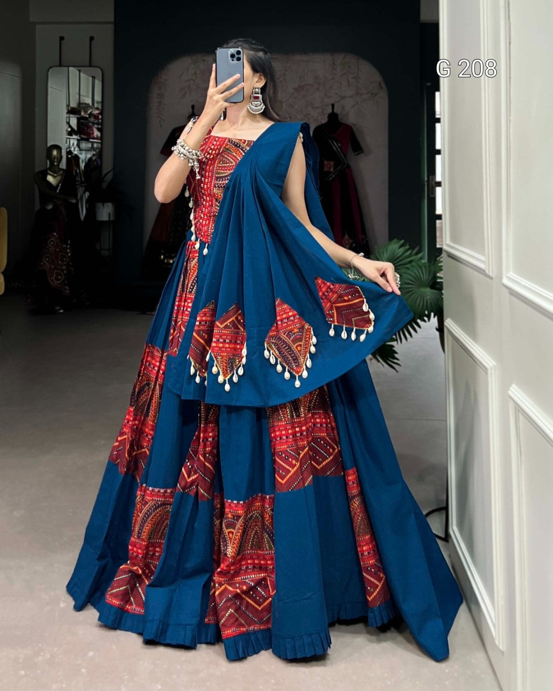 Woman wearing a blue and red traditional outfit with a cape, standing in a room.