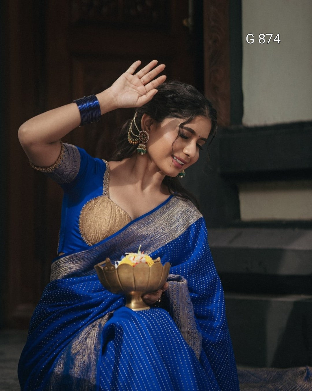 Woman in a blue saree holding a brass bowl with a candle, traditional attire.