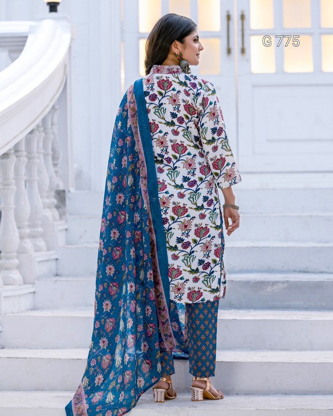 Woman in a floral outfit with a blue dupatta standing on white steps.