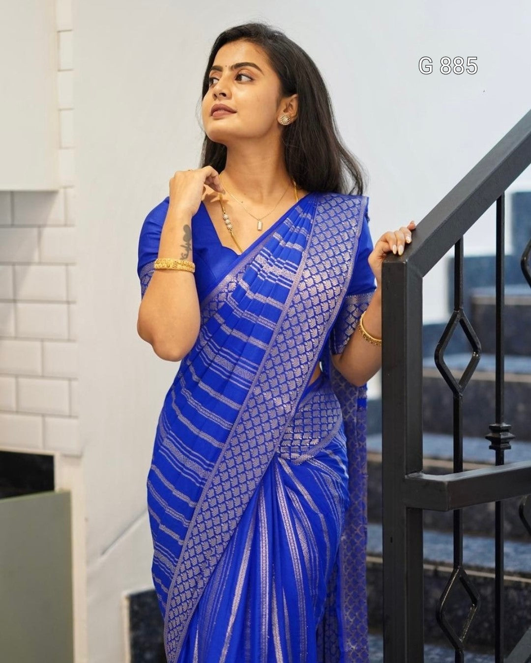 Woman wearing a blue saree with a white pattern, standing indoors.
