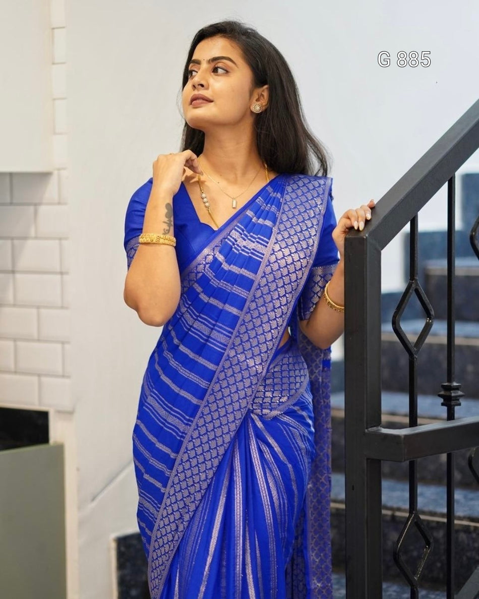 Woman wearing a blue saree with a white pattern, standing indoors.