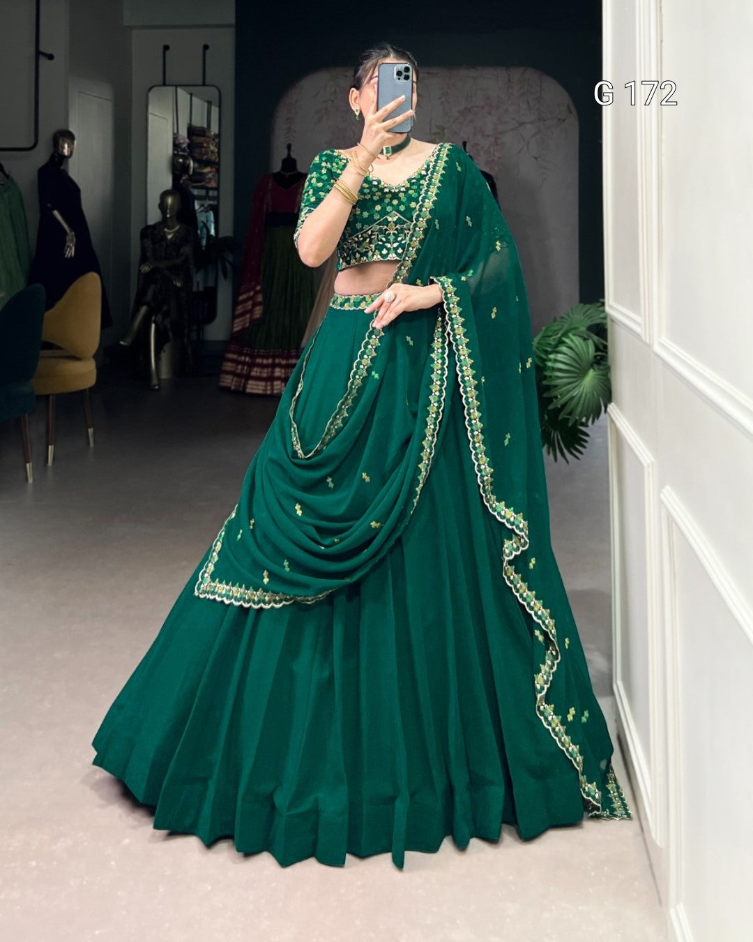 Person wearing a green traditional outfit with gold embroidery in a room.