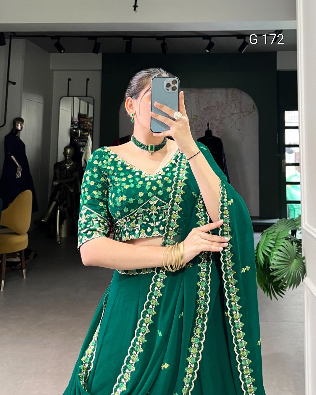 Person wearing a green traditional outfit with intricate designs, standing in a room.
