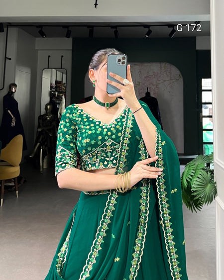 Person wearing a green traditional outfit with intricate designs, standing in a room.