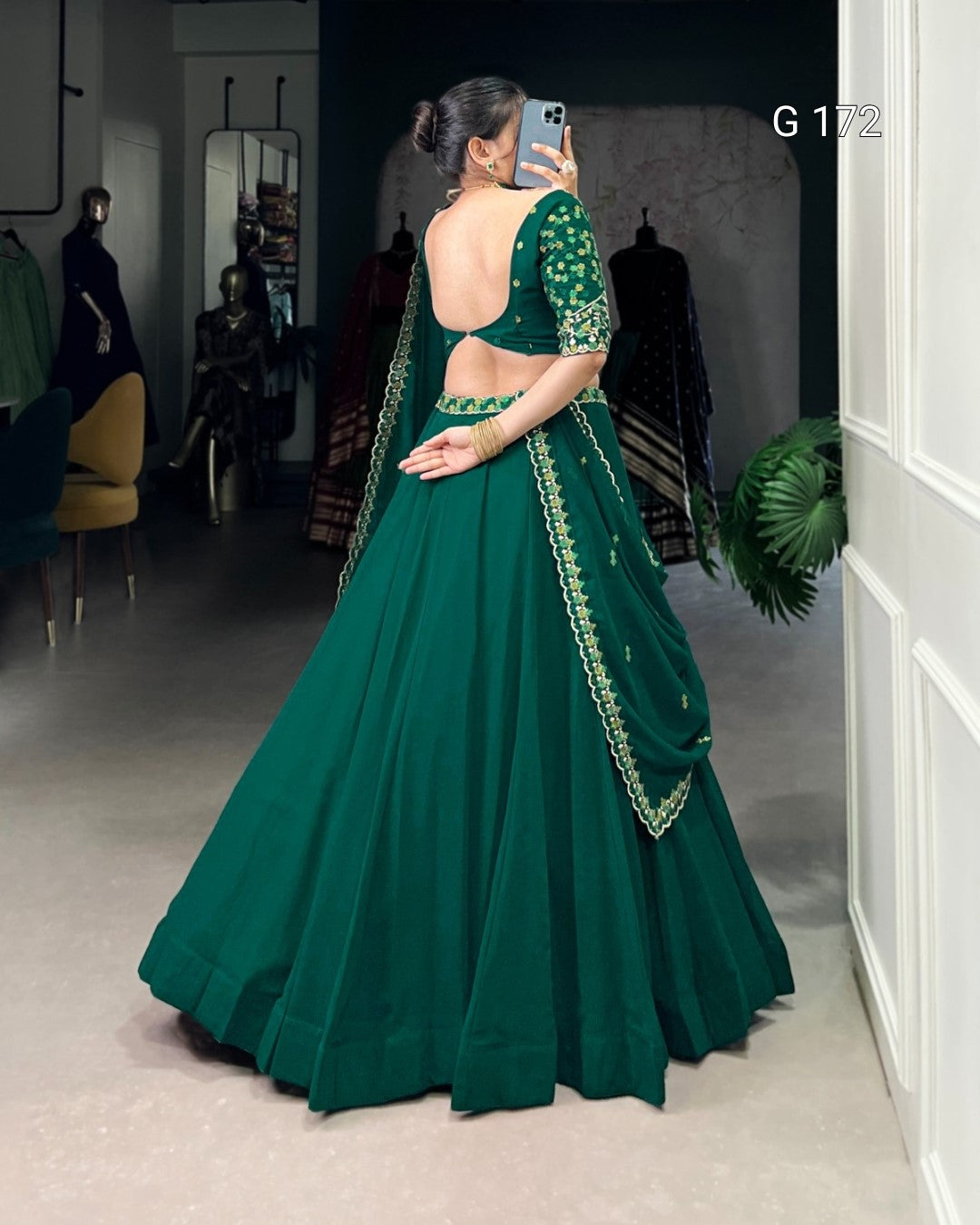 Woman in a green traditional outfit with gold embroidery, standing in a room.