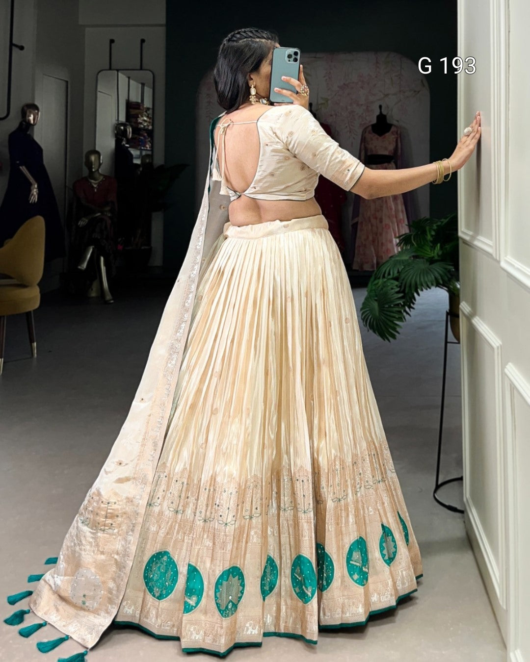 Woman in a traditional outfit with a long skirt and open back, standing in a room with mirrors and clothing.