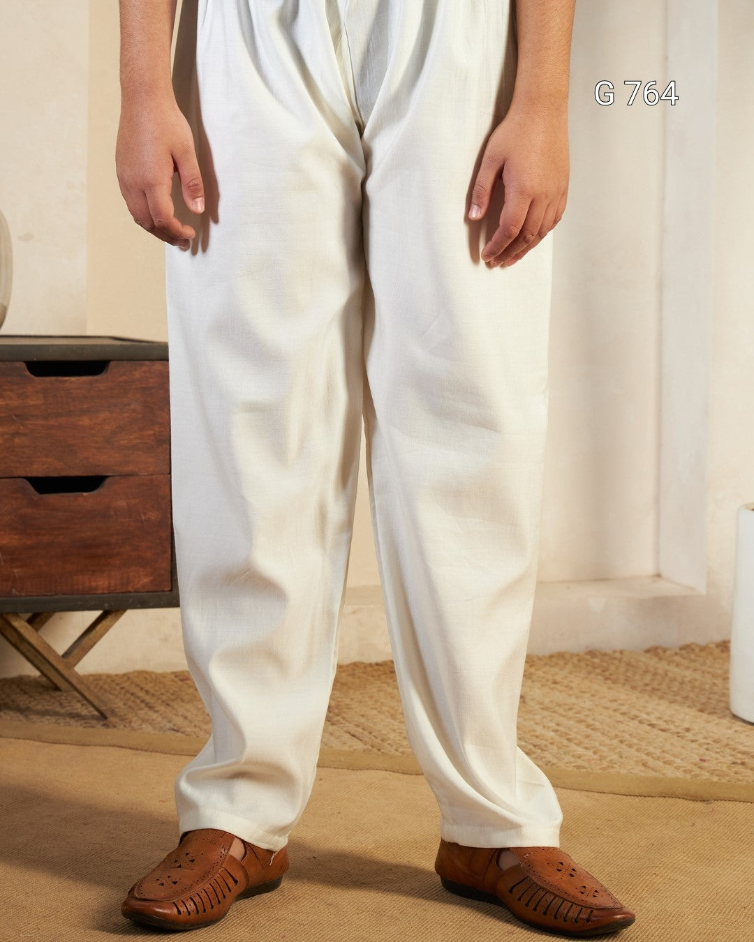 Person wearing white pants and brown sandals in a room with wooden furniture and a curtain.