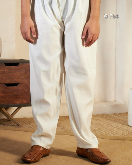 Person wearing white pants and brown sandals in a room with wooden furniture and a curtain.