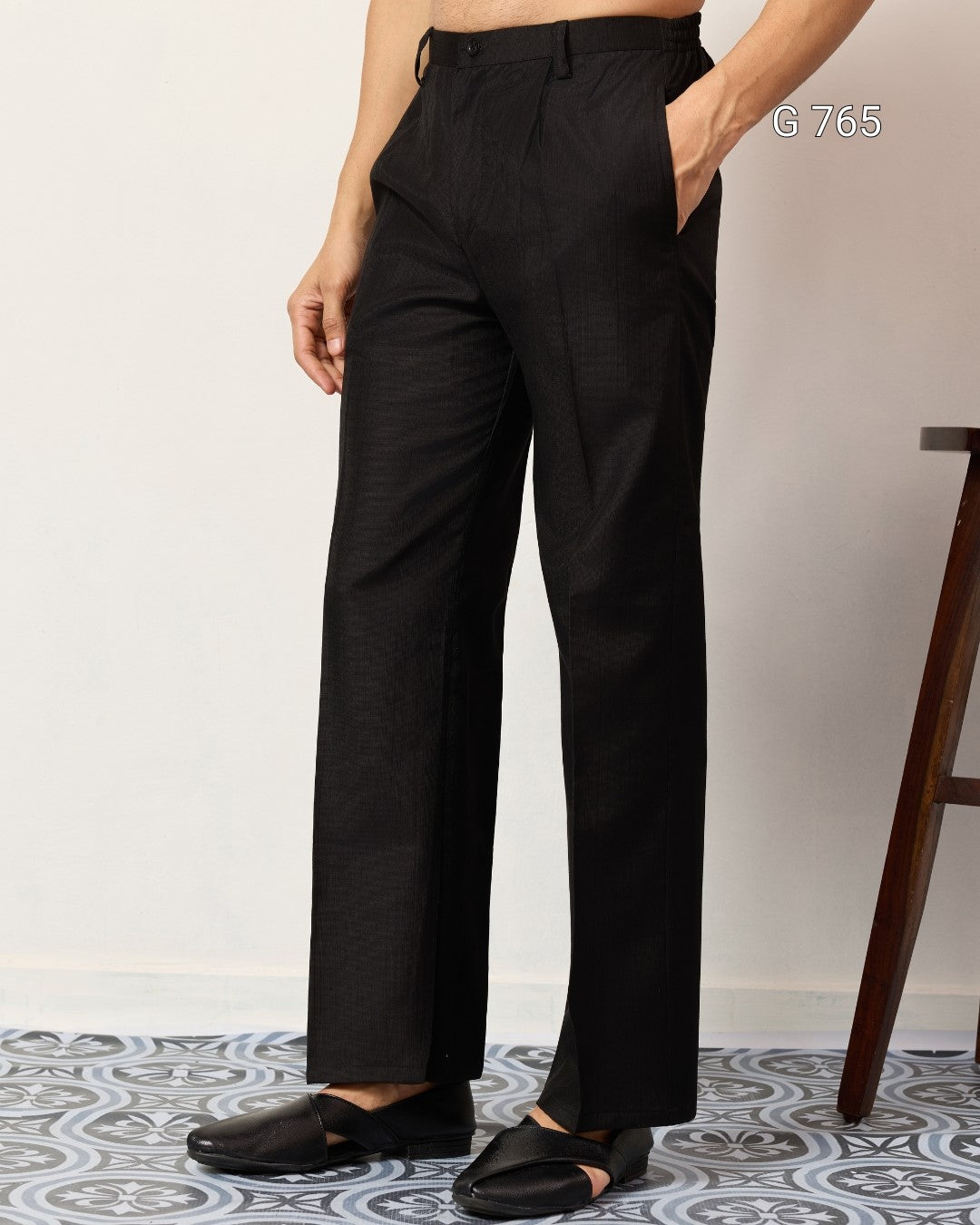 Person wearing black pants standing on a patterned floor with a plain background