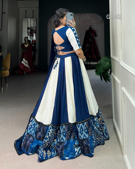 Woman wearing a blue and white traditional outfit with intricate patterns, standing in a room.
