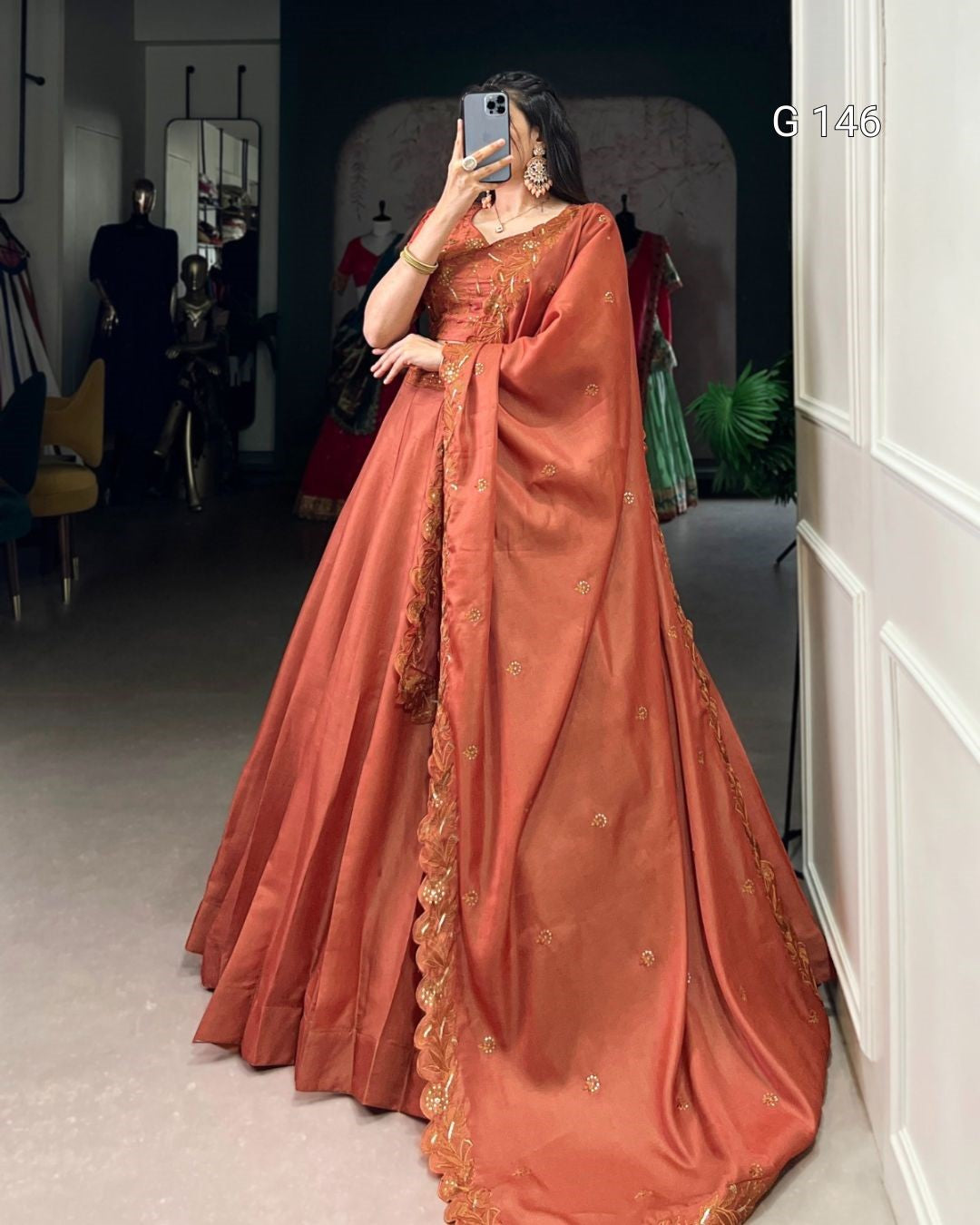Person wearing a traditional orange saree with gold details in an indoor setting.