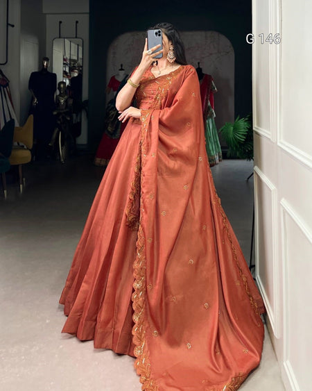 Person wearing a traditional orange saree with gold details in an indoor setting.