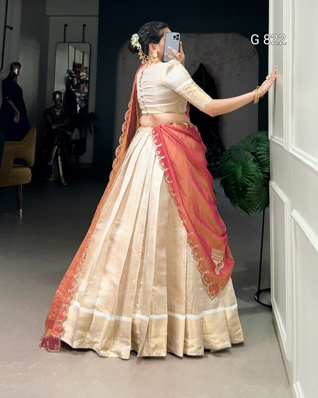 Woman in a traditional outfit with a red and beige sari, standing in a room.