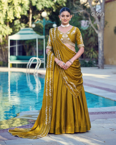 A woman models a mustard yellow ethnic lehenga choli set with white embroidery, standing by a swimming pool in an outdoor setting.