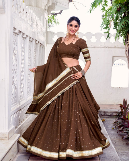 Woman wearing a traditional brown saree with gold accents in an outdoor setting.