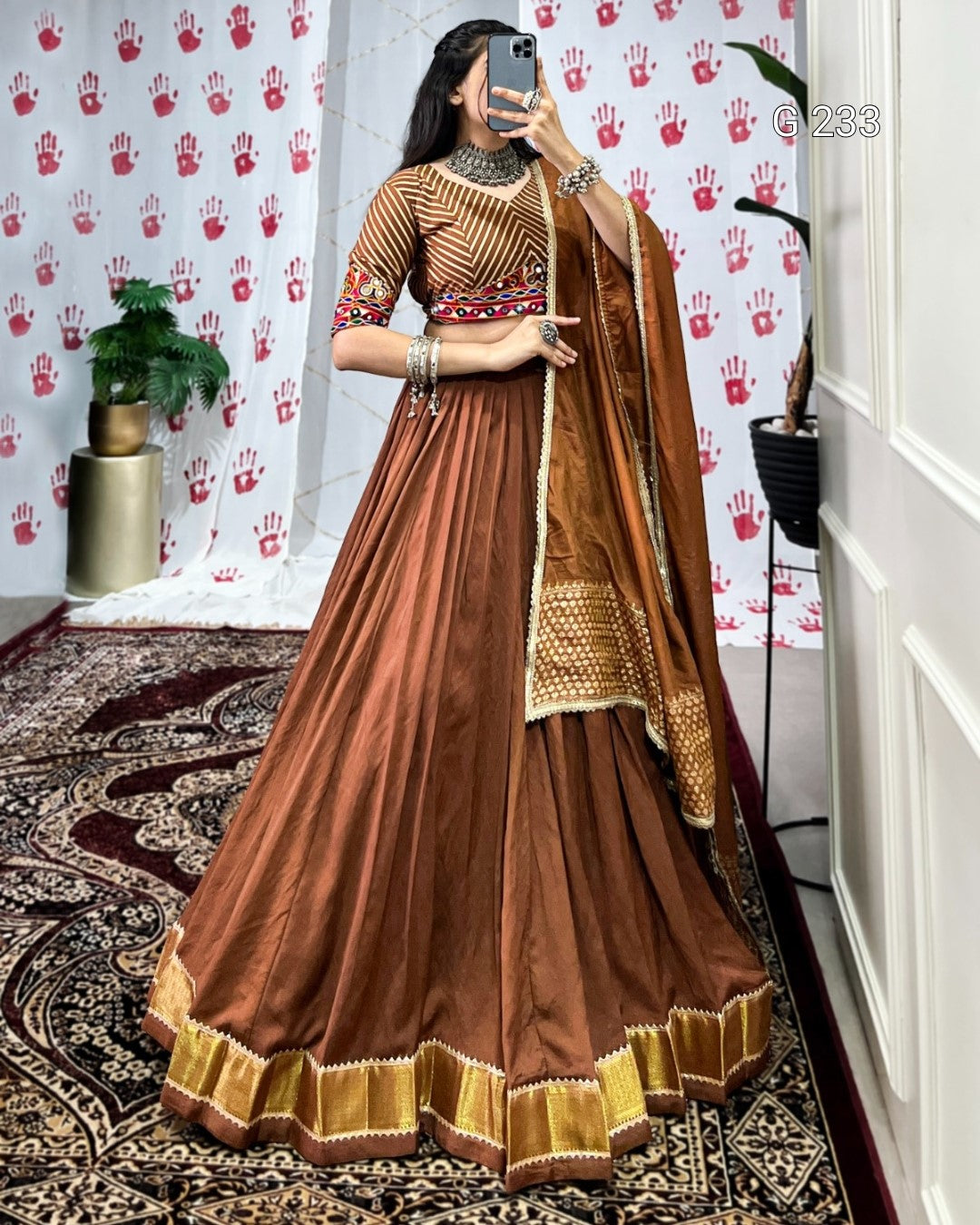Woman taking a mirror selfie wearing a brown traditional outfit with gold details.