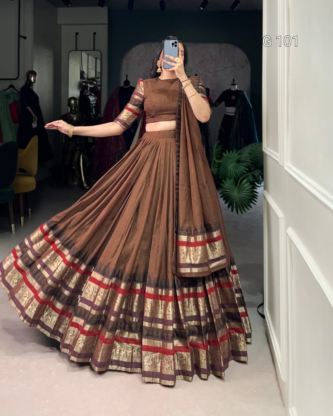 Woman wearing a brown and red plaid dress in a room with mirrors and plants.