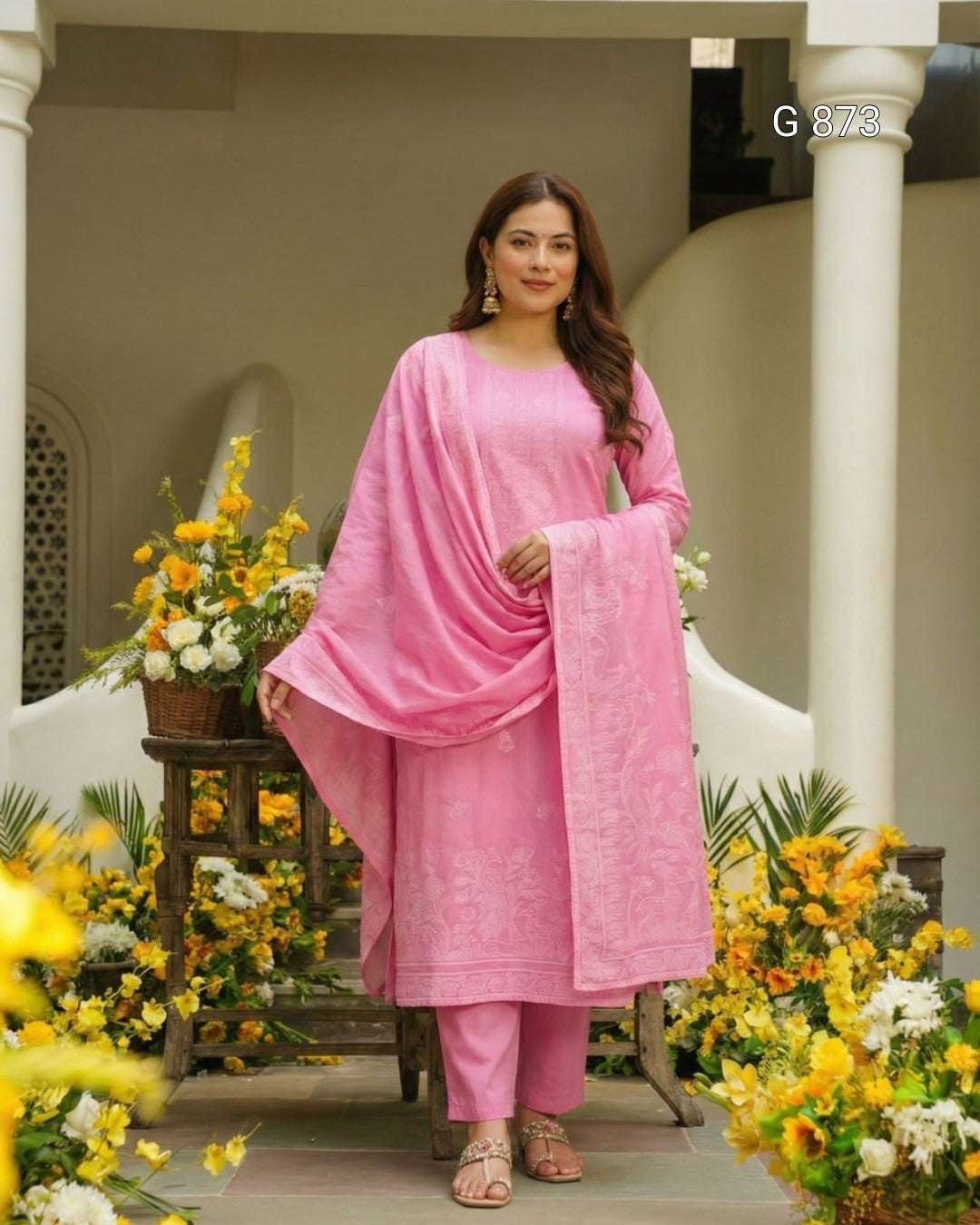 Woman in a pink traditional outfit standing in front of decorative flowers and columns.