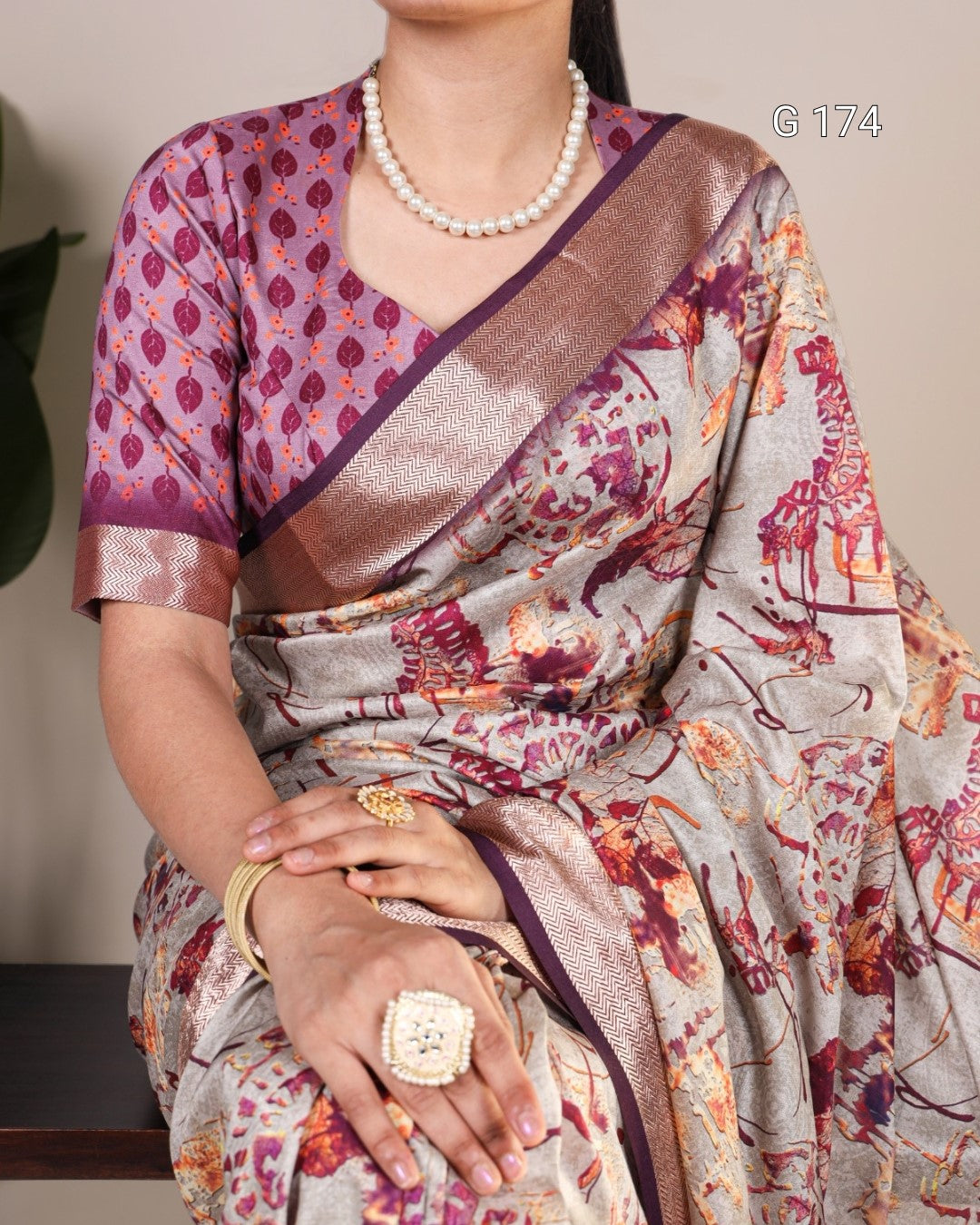 Woman wearing a patterned saree with a pearl necklace and gold jewelry.