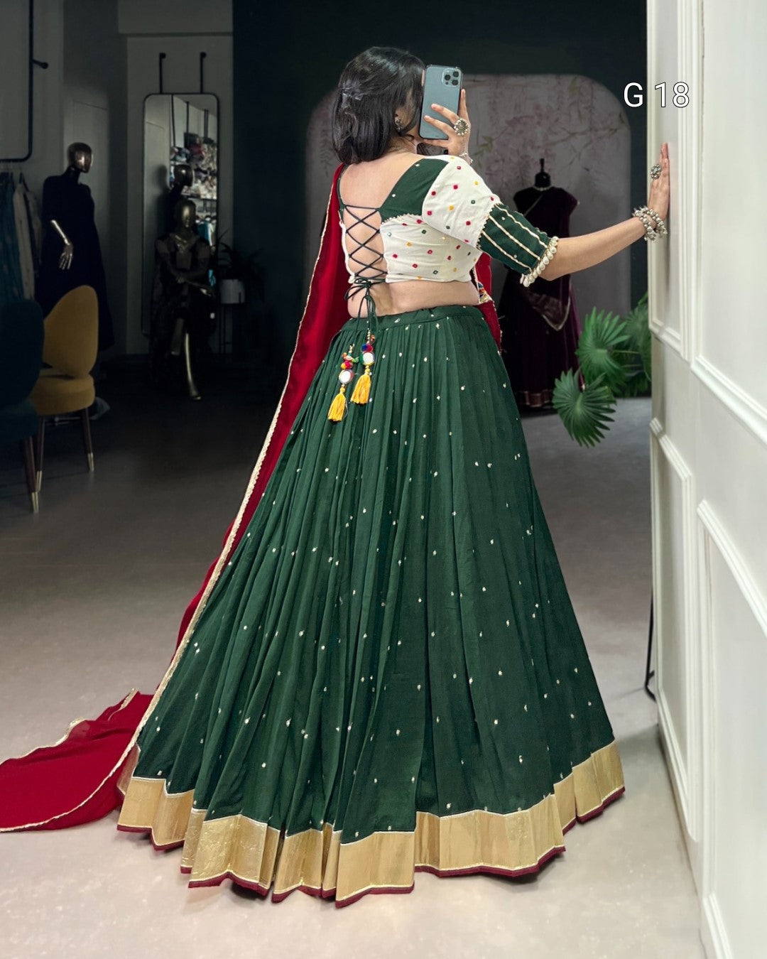 Woman taking a mirror selfie wearing a green and red traditional outfit.