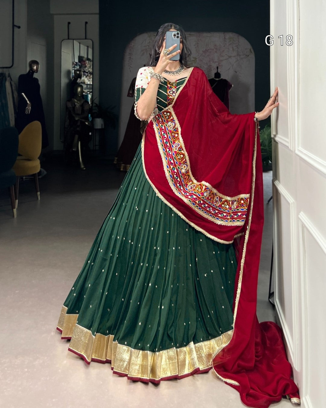 Person wearing a green and red traditional outfit with a saree in a room.
