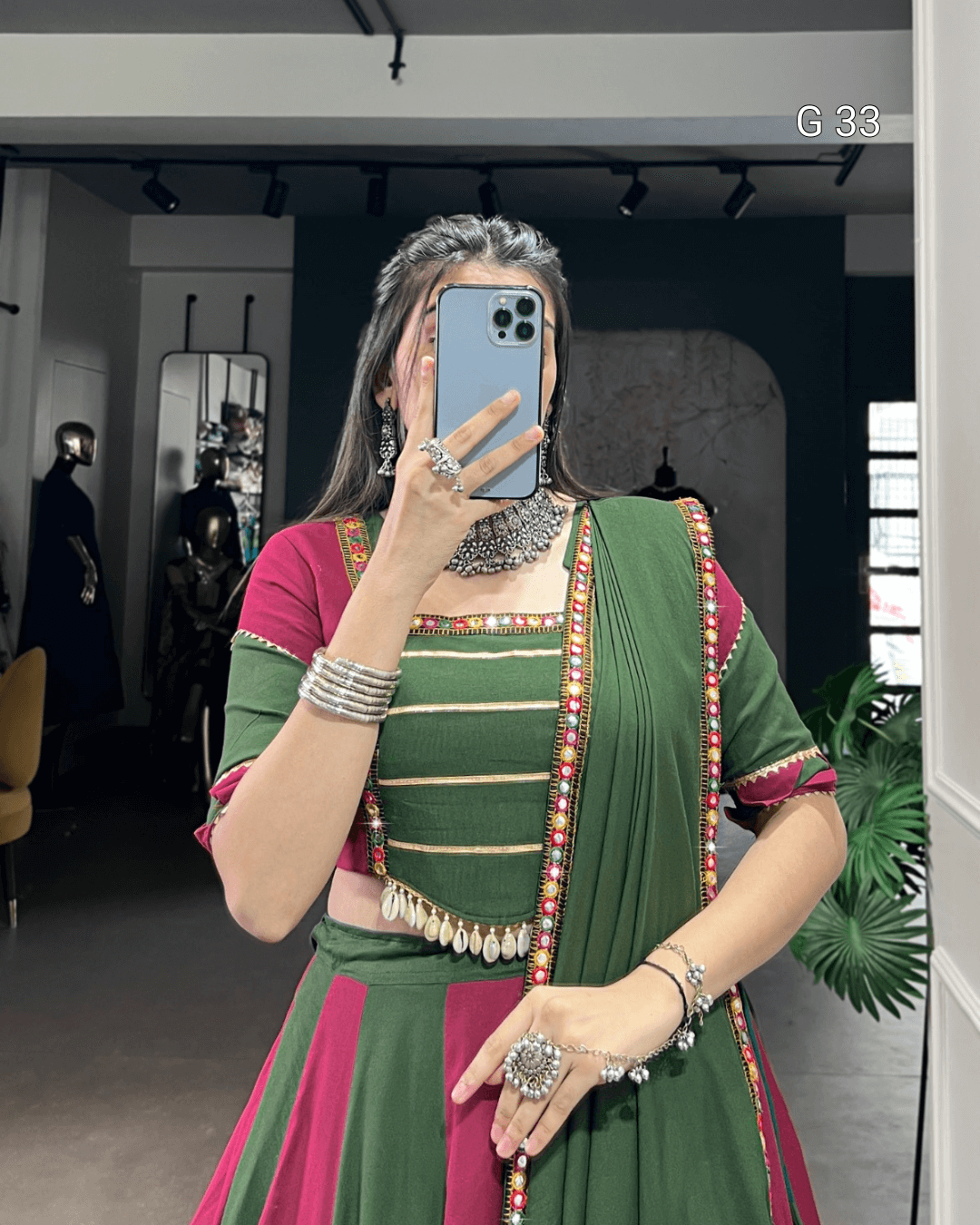 Person wearing a green and pink traditional outfit with jewelry indoors.