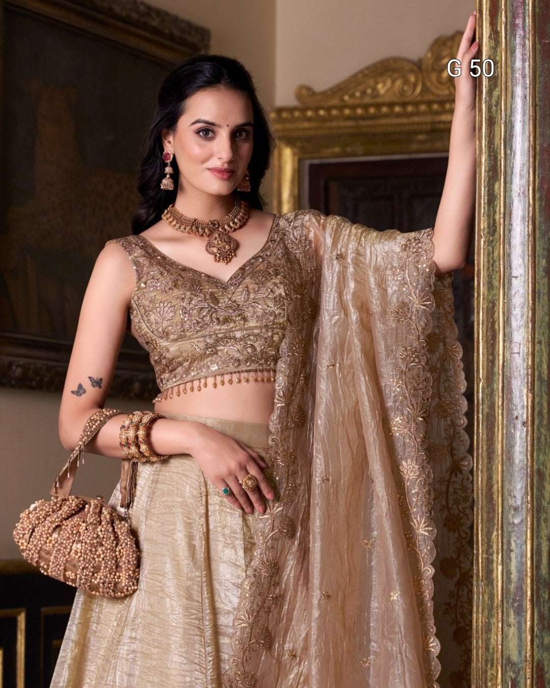 Woman in a traditional outfit with gold and beige colors, holding a matching handbag.