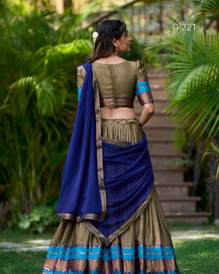 Woman in traditional green and blue saree standing outdoors with greenery in the background