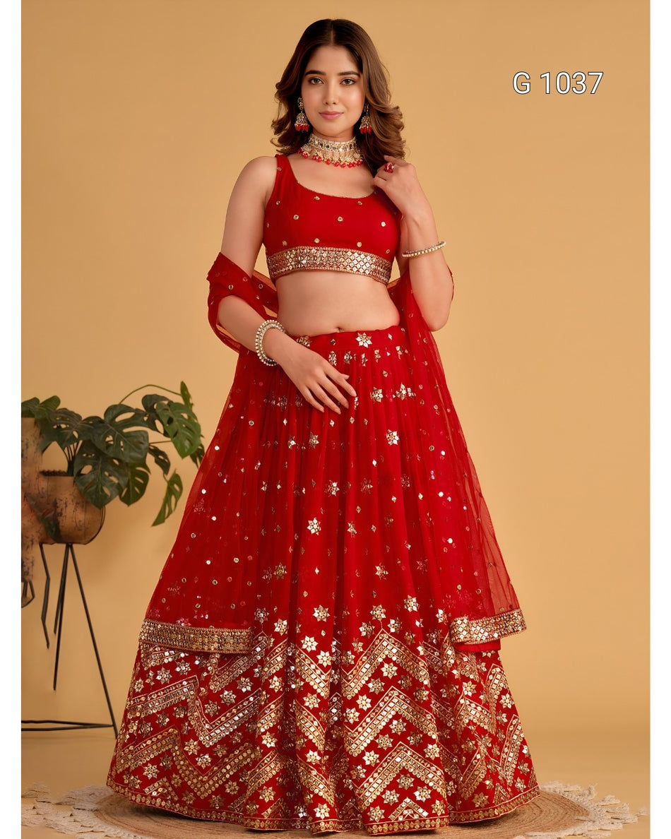 A woman models a red and gold traditional Indian lehenga choli set against a warm beige studio backdrop. The outfit features a red sleeveless blouse with gold embroidery, a matching full skirt with gold floral motifs and border detailing, and a dupatta draped over the shoulder.