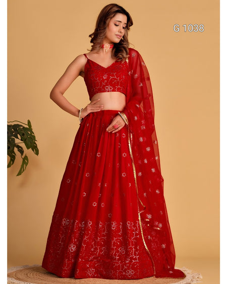 A woman modeling a red embroidered lehenga choli set with a matching dupatta against a solid beige background. The outfit features intricate floral embroidery and has the code 'G 1038' printed in the top right corner.