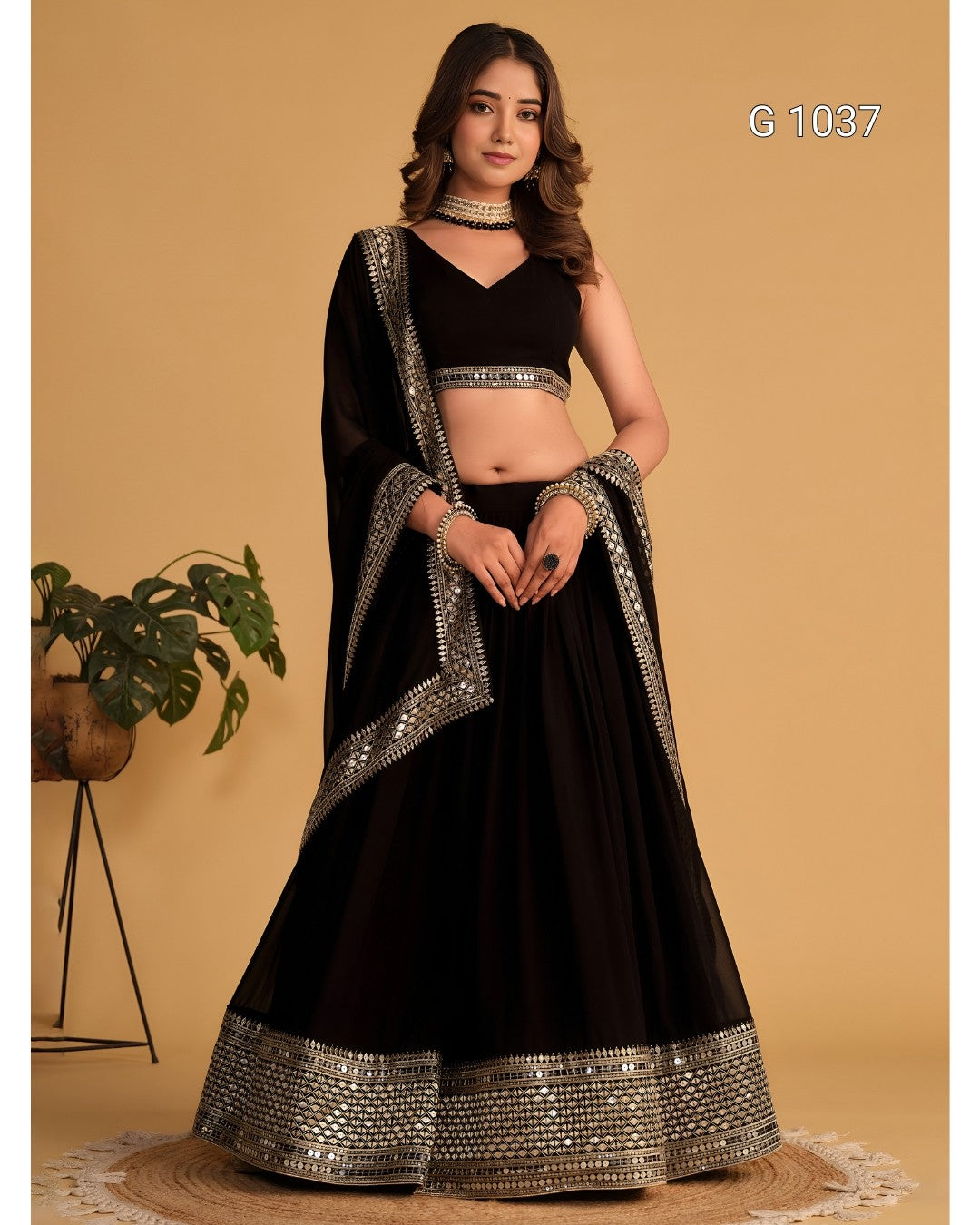 A woman models a black traditional Indian lehenga choli set with silver mirror work borders, standing against a solid beige background.