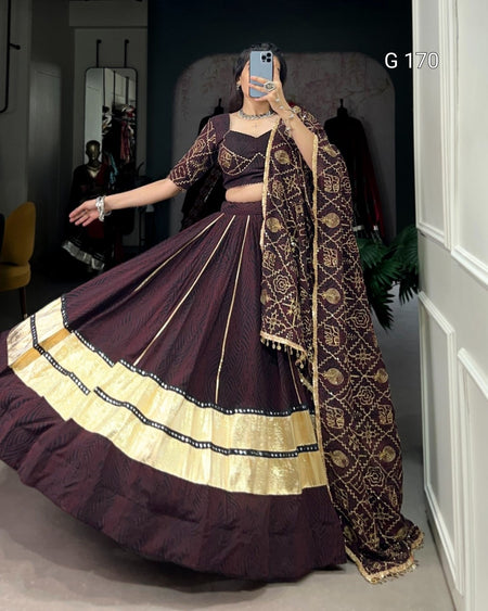 Woman wearing a traditional outfit with a dark purple lehenga and gold details, standing in a room.