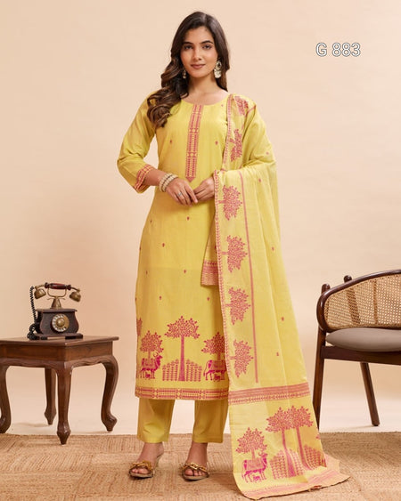 Woman wearing a yellow embroidered traditional outfit with a pink border in a room setting.