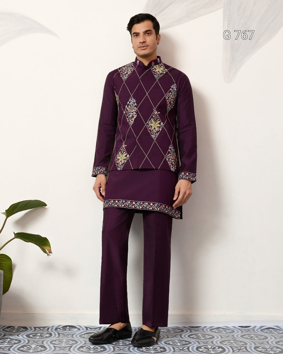 Man wearing a traditional embroidered outfit against a white wall.