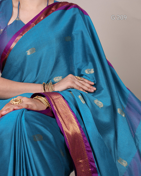 Blue saree with gold patterns and a hand wearing gold jewelry on a neutral background
