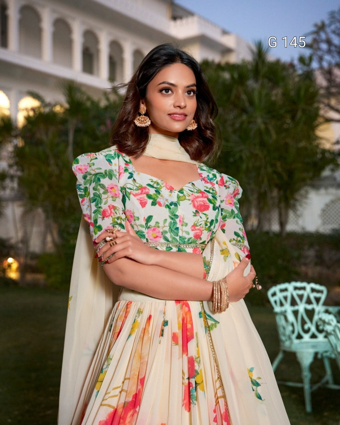 Woman in a floral dress standing outdoors with greenery and a building in the background
