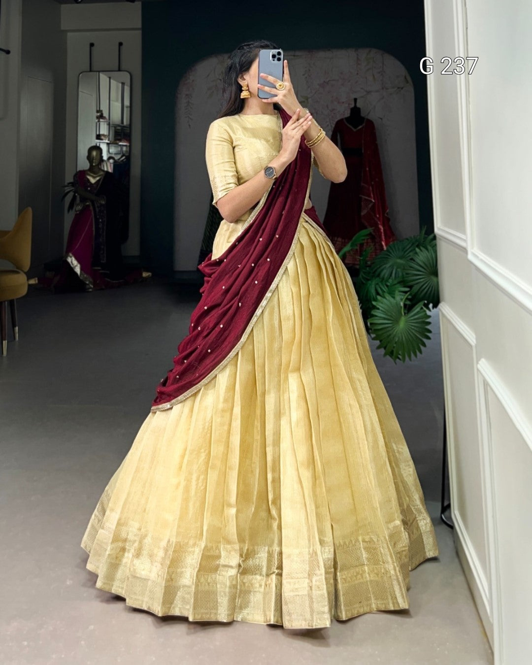 Woman wearing a yellow saree with a maroon border, standing in a room.