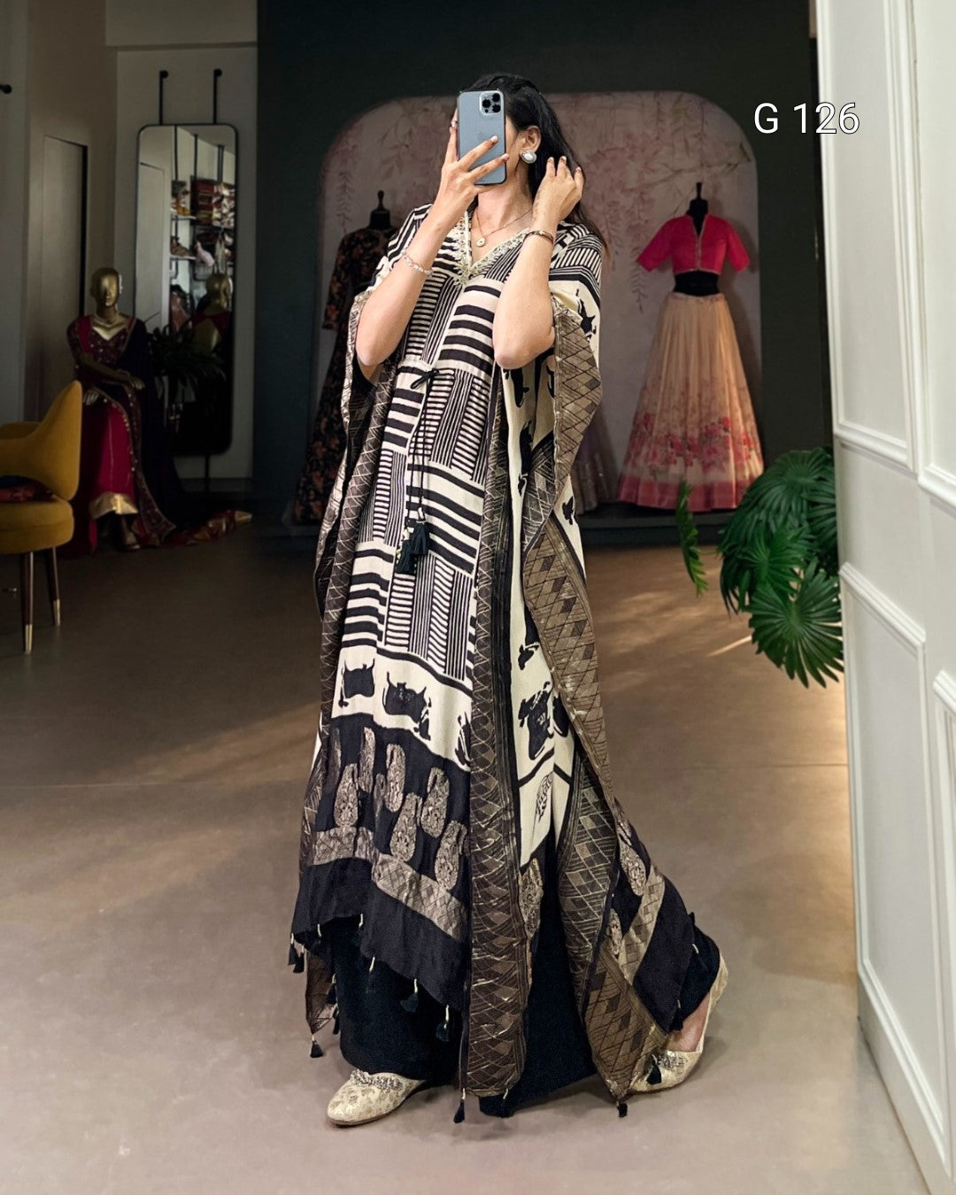 Woman taking a mirror selfie wearing a long, patterned dress in a store setting.