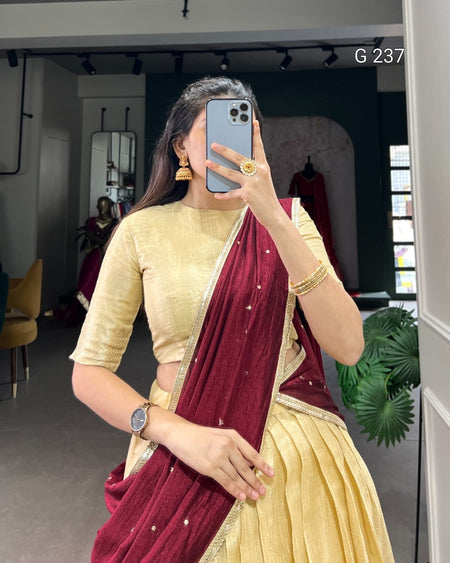 Woman taking a mirror selfie wearing a gold blouse and maroon saree in an indoor setting.