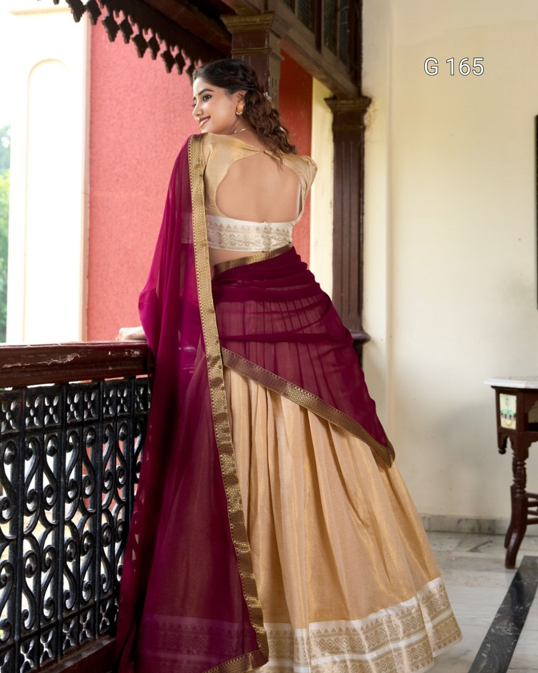 Woman wearing a maroon and beige saree with a traditional setting.