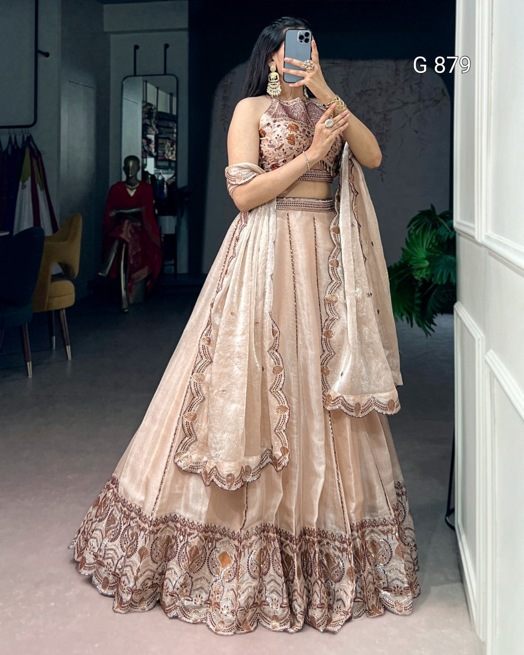 Woman in a beige and brown embroidered traditional outfit taking a mirror selfie.