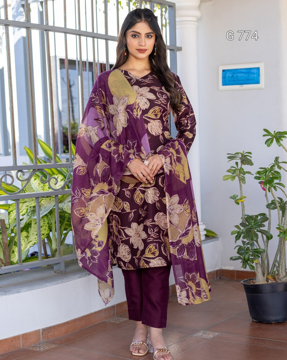 Woman wearing a purple floral outfit standing in front of a building with plants.