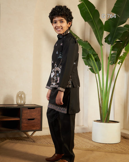 Child wearing a black traditional outfit with embroidery in a room with a plant and wooden cabinet.