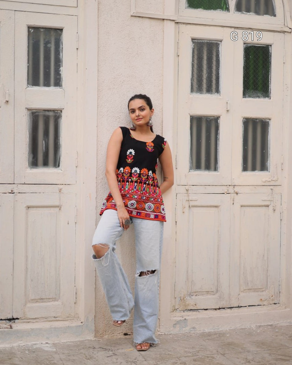 Woman wearing a black top with floral design and light blue jeans standing in front of a white door.
