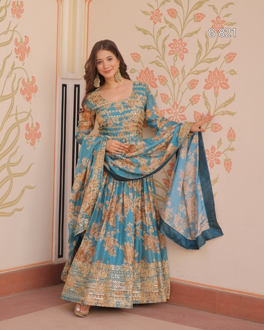 Woman in a blue and gold traditional outfit standing against a decorative wall.